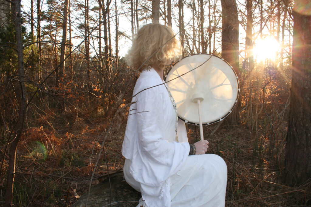 Yogalärare med trumma, i en skogsdunge. Solen lyser genom rumman och skapar en bild av ett nät.