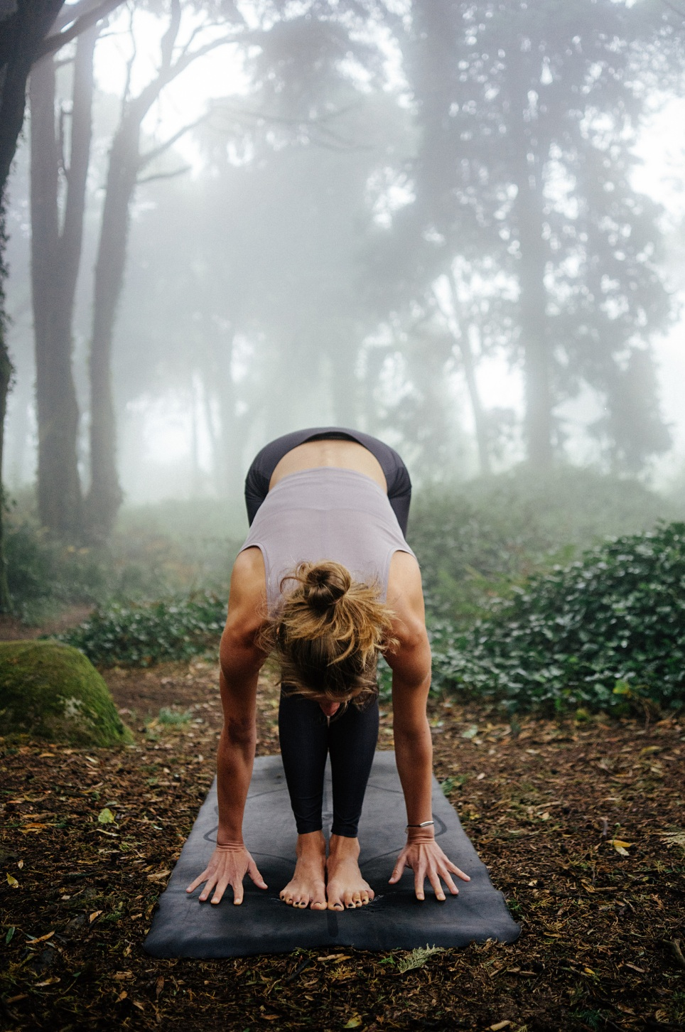 kvinna som gör yoga i skogen. framåtfällning. dimma syns i bakgrunden.